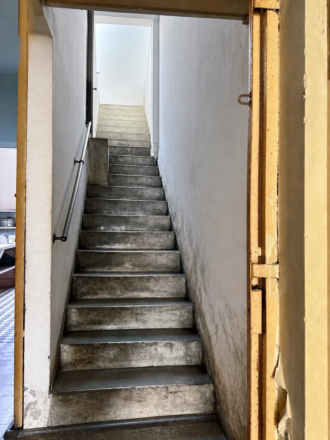Cầu thang bê tông từ tầng trệt dẫn lên gác lửng — lối tiếp cận duy nhất tới khu vực đặt hầm bí mật.