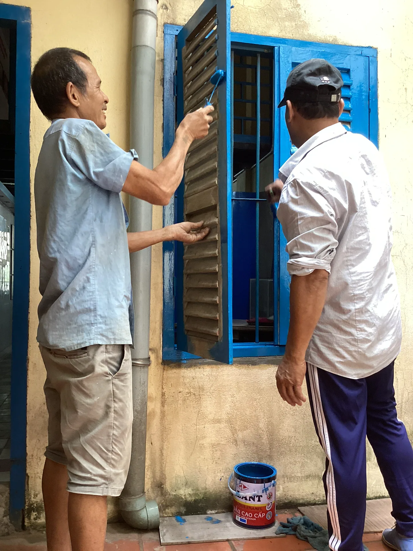 Nhân công đang sơn, sửa khung cửa sổ màu xanh tại khu nhà di tích.