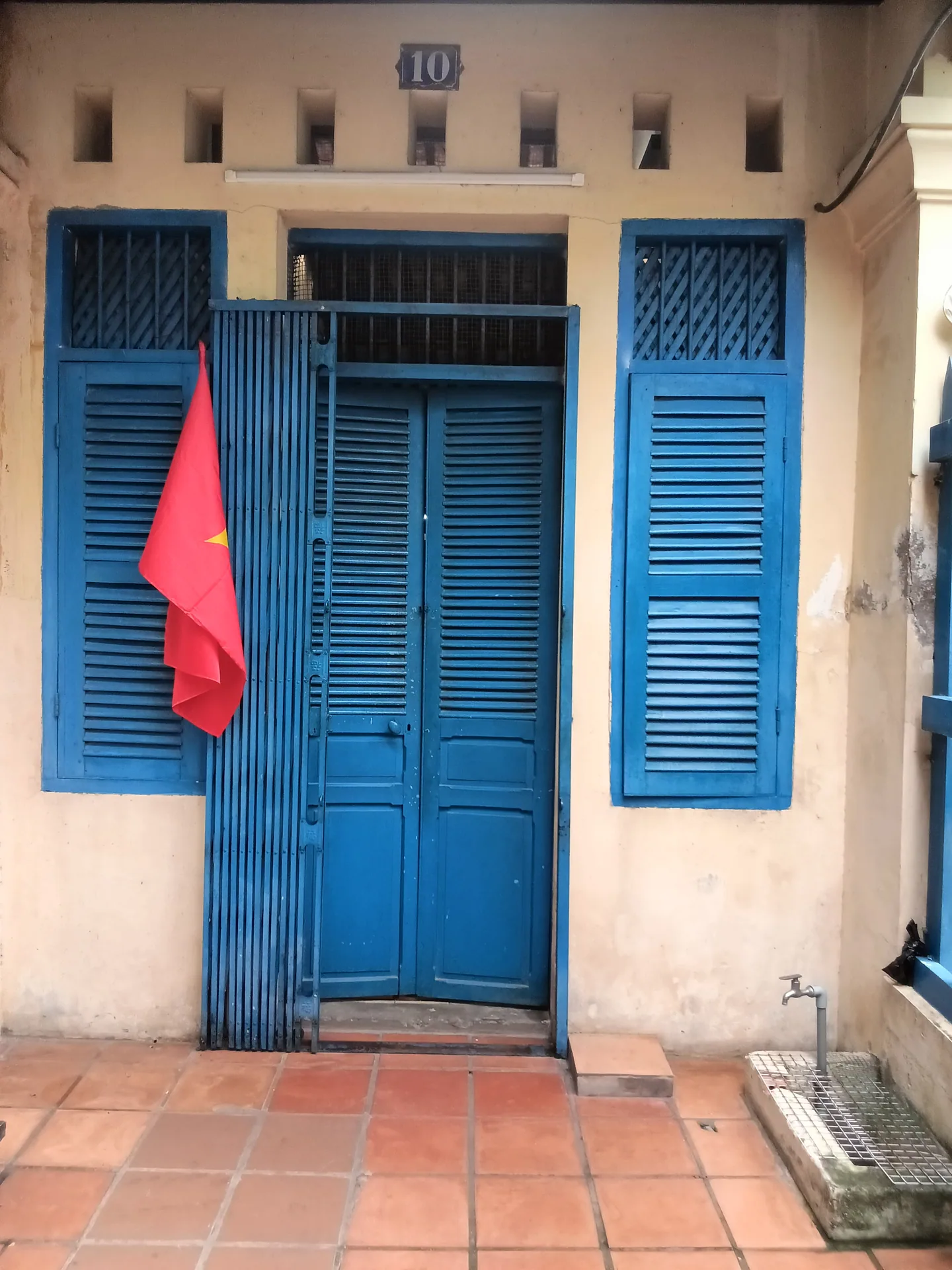 Mặt cửa xanh của căn nhà di tích, có lá cờ đỏ treo phía trước.