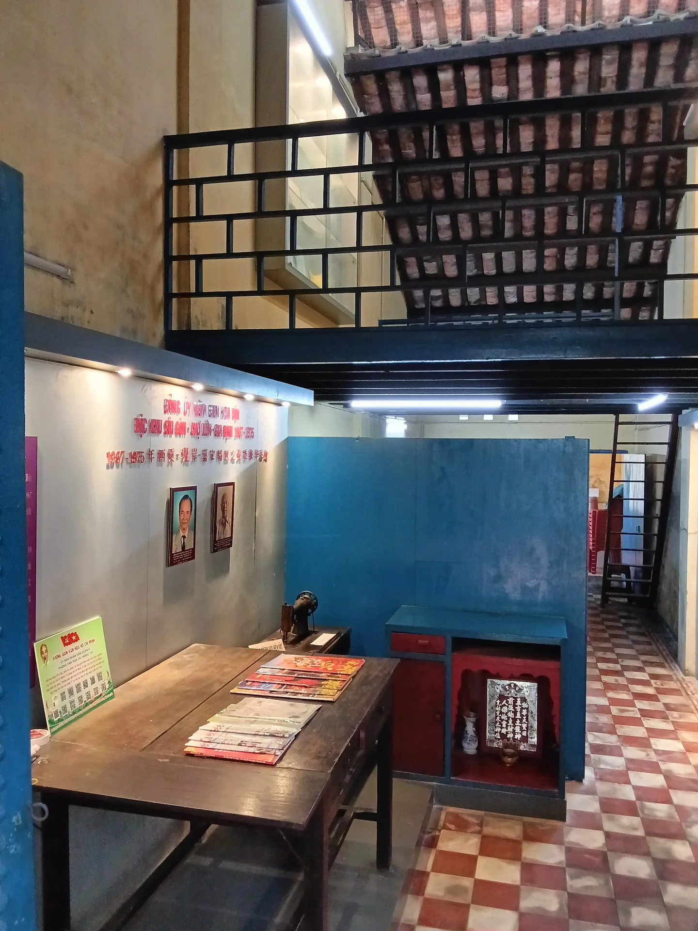 Không gian nội thất nhà di tích với bàn trưng bày, tường thông tin và nền gạch caro.