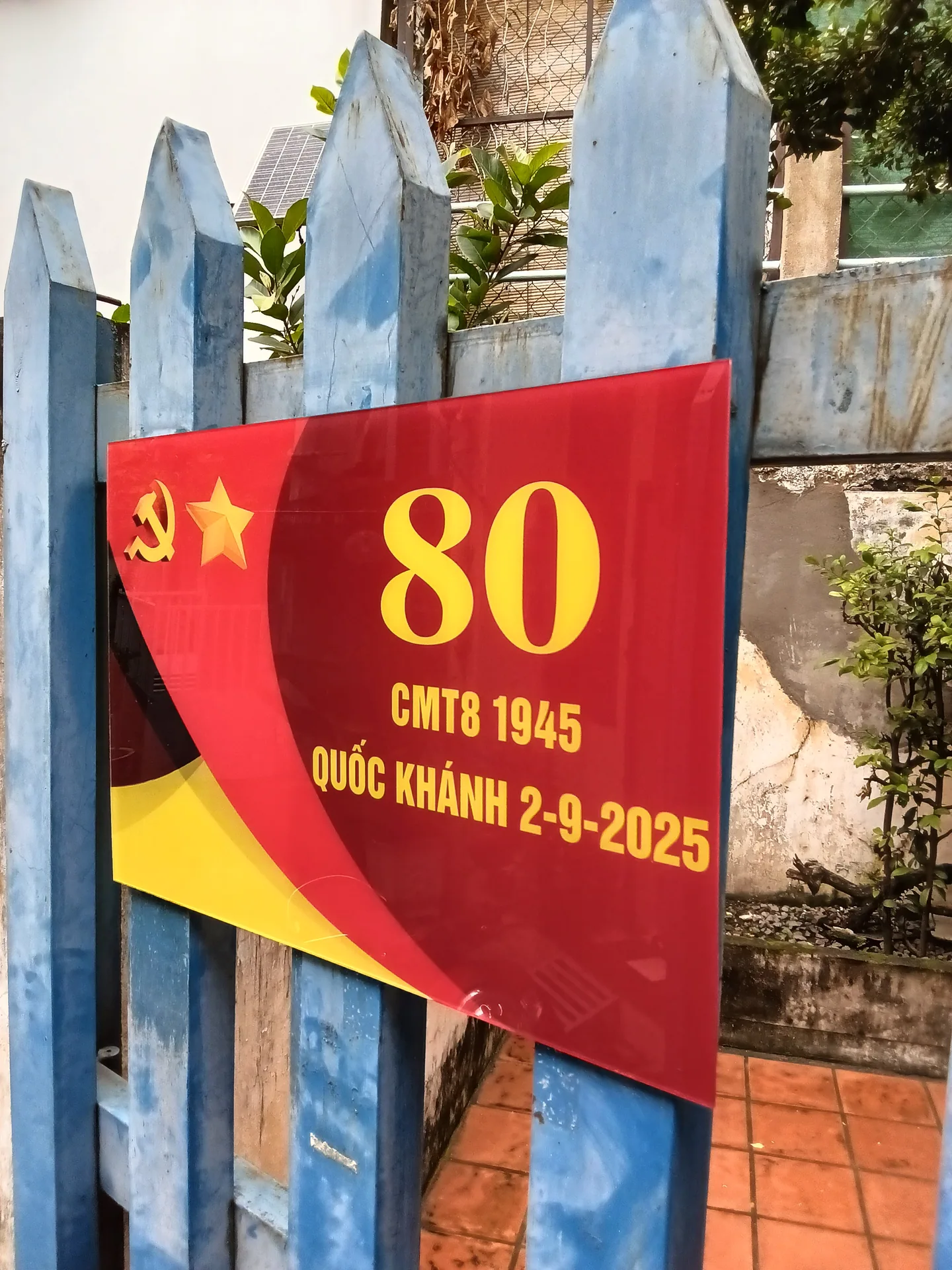 Băng rôn đỏ kỷ niệm 80 năm Cách mạng Tháng Tám 1945 và Quốc khánh 2-9-2025 gắn trên hàng rào xanh.